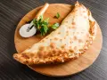 Złocisty calzone, czyli włoska pierożkowa pizza, leży na desce z krążkiem do pizzy i natką pietruszki.