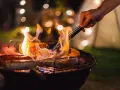Wieczorne grillowanie: kiełbaski, steki i kukurydza skwierczą na ogniu, a ręka z szczypcami obraca mięso.