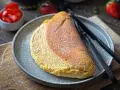 Puszysty omlet, lekko przyprószony cukrem pudrem, czeka na talerzu obok czarnych sztućców. W tle miseczka z truskawkami.