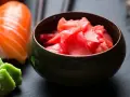 Miseczka z różowym, marynowanym imbirem obok sushi i wasabi. Idealny dodatek do japońskich potraw.