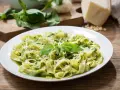 Talerz tagliatelle z aromatycznym pesto z rukoli, posypany parmezanem i udekorowany listkami bazylii.