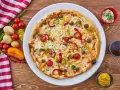 Pizza z mięsem mielonym, pomidorkami, papryką i kukurydzą na białym talerzu, obok sosy i warzywa.