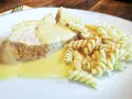 Kawałek pieczonego mięsa w kremowym sosie potrawkowym, podany z makaronem fusilli.