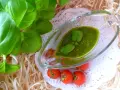 Świeże liście bazylii i pomidorki koktajlowe obok sosu pesto z bazylii w szklanym naczyniu.