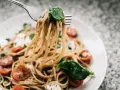 Widelec podnosi porcję spaghetti z pomidorkami i mozzarellą. Czy makaron to węglowodany? Tak, to pyszne źródło energii!
