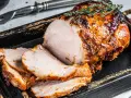 Soczysty schab pieczony w piekarniku w naczyniu, pokrojony w plastry, ozdobiony gałązką rozmarynu.