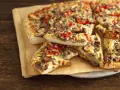 Grube ciasto na pizze z kiełbasą, pieczarkami i papryką, podane na papierze do pieczenia.