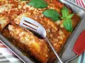 Zapiekana tortilla z mięsem mielonym, polana sosem pomidorowym i posypana serem, ozdobiona listkami bazylii.