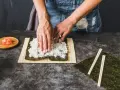 Ręce rozkładają ryż na nori, przygotowując zaprawę do sushi na 500g ryżu. Obok leżą pałeczki i imbir.