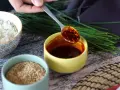 Łyżka z aromatycznym sosem gochujang, obok miseczki ryżu, sezamu i szczypiorku.