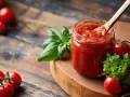 Słoik domowego sosu pomidorowego z bazylią i pomidorkami koktajlowymi. Idealny do pizzy, makaronu, a nawet jako dodatek do pieczonych mięs. Pyszny sos cebulowy w tle.