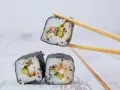 Trzy kawałki sushi z ryżem, ogórkiem i rybą, jeden podniesiony pałeczkami. Idealne do sosu, który stanowi zalewa do sushi.