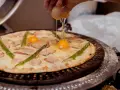 Ktoś dodaje jajko do pizzy z boczkiem i szparagami. Pyszna pizza z jajkiem w przygotowaniu.