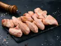 Skrzydełka kurczaka gotowe do pieczenia, zamarynowane w aromatycznej solance. Obok młynek do pieprzu i gruboziarnista sól.
