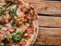 Pyszna pizza carbonara z chrupiącym boczkiem i rukolą, podana na drewnianym blacie.