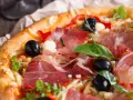 Pyszna pizza z cienko pokrojoną, aromatyczną szynką, czarnymi oliwkami i papryką. Idealna jaka szynka na pizzę!
