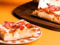 Kawałek pysznej pizzy rzymskiej z szynką i ciągnącym się serem na talerzu, obok reszta na desce.