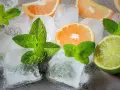 Jak zrobić krystaliczny lód w domu? Kostki lodu, plasterki pomarańczy, limonki i listki mięty tworzą orzeźwiającą kompozycję.
