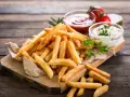 Złociste frytki na desce, idealne co do frytek na szybko. Obok ketchup i majonez.