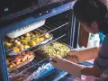 Ktoś wkłada do piekarnika naczynie z zapiekanką. W środku pieką się ziemniaki i marchewka. Ciekawe, podgrzewanie w piekarniku ile stopni?