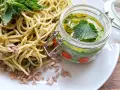 Makaron z pesto z pokrzywy, ozdobiony świeżymi liśćmi pokrzywy i pestkami słonecznika. Obok słoiczek z domowym pesto.