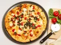Pyszna pizza z serka wiejskiego, pomidorkami koktajlowymi i bazylią. Obok leży krajalnica do pizzy i świeże pomidory.