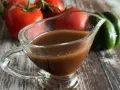 Sos balsamiczny w sosjerce, w tle pomidory i zielona papryka. Idealny do sałatek i mięs.