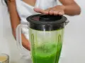 Ręka dociska pokrywę blendera z zielonym koktajlem z jarmużu.