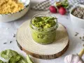 Pesto z liści rzodkiewki w słoiczku, ozdobione natką pietruszki, na drewnianym krążku. Obok czosnek, rzodkiewki i nasiona.