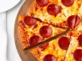 Kawałki pizzy z serem i okrągłymi plasterkami peperoni, ułożone na drewnianej desce.