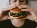 Osoba trzyma soczystego burgera, zastanawiając się, ile kalorii ma burger w restauracji.