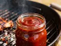 Słoik gęstego, aromatycznego sosu z żeberek paruje na grillu obok pieczonych mięs. Idealny dodatek do letniego grillowania.