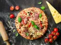 Gotowa pizza z salami, serem i warzywami, obok wałek, pomidorki i ser. Idealna na wieczór z przyjaciółmi, gdy brakuje czasu na przygotowanie ciasta z mąki na pizzę.
