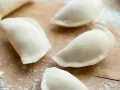 Surowe pierogi uformowane na drewnianej desce. To ciasto na pierogi bez jajka, gotowe do nadzienia.