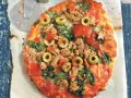 Pyszna pizza z tuńczykiem, szpinakiem i oliwkami, gotowa do pokrojenia.