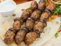 Kofta kebab z bakłażanem na płaskim chlebie, podany z sosem.
