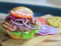 Soczysty burger z chrupiącym boczkiem, pomidorem, sałatą i czerwoną cebulą. Dodatki do burgera kuszą smakiem.