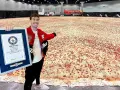 Mężczyzna prezentuje certyfikat Guinnessa za największą pizzę świata, która rozciąga się na ogromnej przestrzeni.