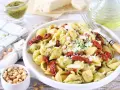 Pyszny makaron z pesto i suszonymi pomidorami, posypany parmezanem i orzeszkami pinii.
