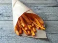 Chrupiące frytki z marchewki w papierowym rożku, ułożone na drewnianym blacie.