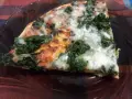 Kawałek pysznej pizzy ze szpinakiem, z ciągnącym się serem i pomidorowym sosem, na ciemnym talerzu.
