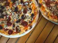 Dwie pizze z bogactwem składników na wierzchu: salami, pieczarki i czarne oliwki. Idealne na wspólny posiłek.
