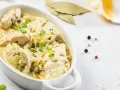 Pyszny kurczak w sosie serowym, udekorowany szczypiorkiem, podany w białej miseczce.