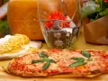 Pyszne rodzaje pizzy, makaron i ser parmezan. W tle szklany wazon z ozdobami i kwiatami.
