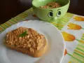 Pyszna pasta z makreli i twarogu na kromce chleba, udekorowana listkiem bazylii. Obok miseczka z pastą i wesołą buźką.