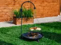 Grill trójnóg z paleniskiem i rusztem, na którym znajdują się kiełbaski, pieczywo i warzywa.