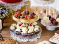 Słodkie przekąski: babeczki, tartaletki z owocami, cake pops i ciasto czekoladowe na drewnianym stole.