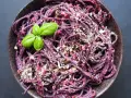 Fioletowy makaron z buraczanym pesto ze słoika, posypany orzechami i udekorowany listkiem bazylii.