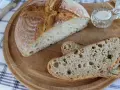 Chleb pszenno żytni na zakwasie, pokrojony na desce, z solniczką i nożem w tle.
