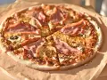Pizza z szynką i pieczarkami, idealna na szybki obiad. Jakie pieczarki do pizzy? Te ciemne, pokrojone w plasterki, świetnie komponują się z serem i wędliną.